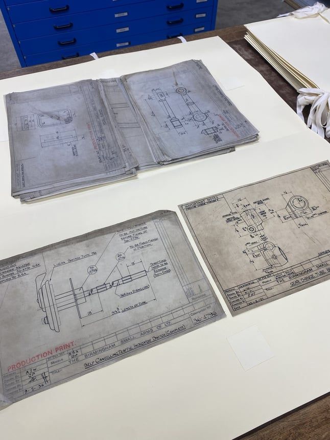 Several technical drawings are laid out on a desk.