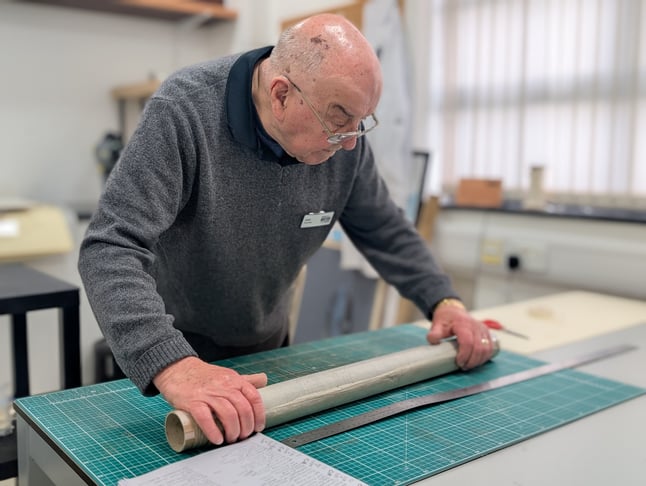 Archive volunteer John Sheffield holds a technical drawing against a steel rule for measuring. He is standing in the Archive's conservation studio.