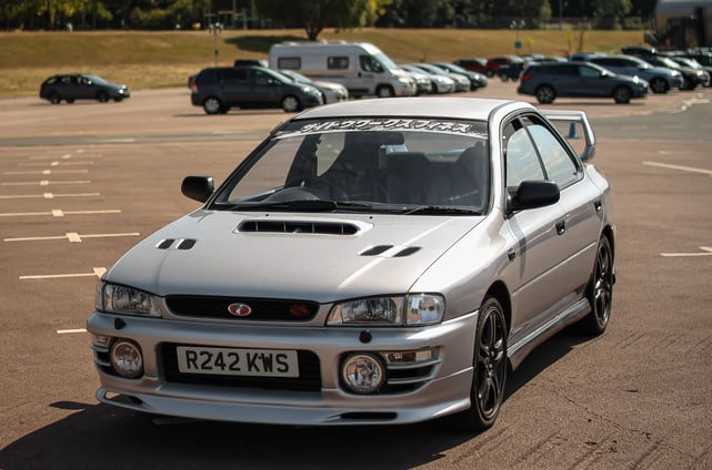 A silver Subaru Impreza situated in a car park. Other cars can be seen in the distance.