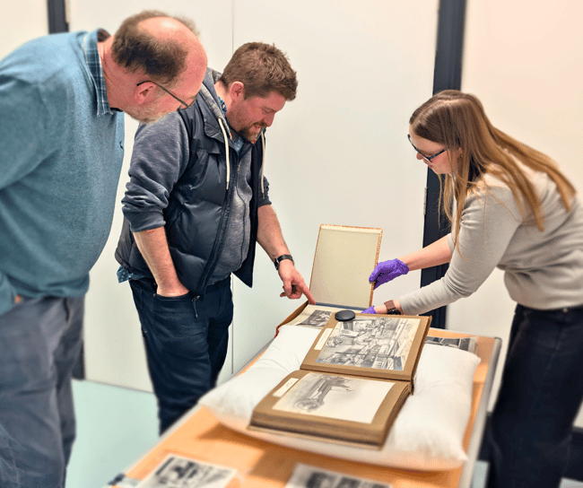 Two gentlemen being shown a historic document by a staff member wearing gloves.