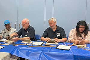 Volunteers Alan and Robin sit at th table and work on their model clay car creations.