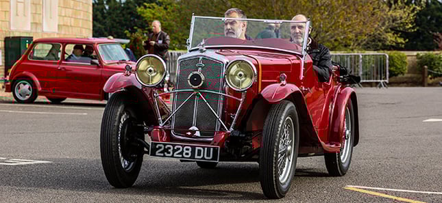 A Member being given a ride in a vintaage MG convertible car painted red