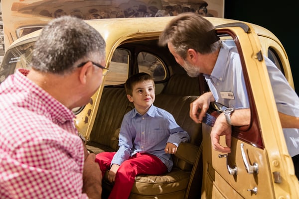 Child sitting in Museum car, finding out about the story from the Museum Attendant.