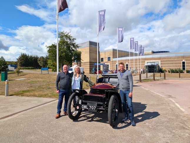 Stephen, Charlotte and Alex stood next to Veteran Car 'OWL' outside the British Motor Museum on a sunny day.