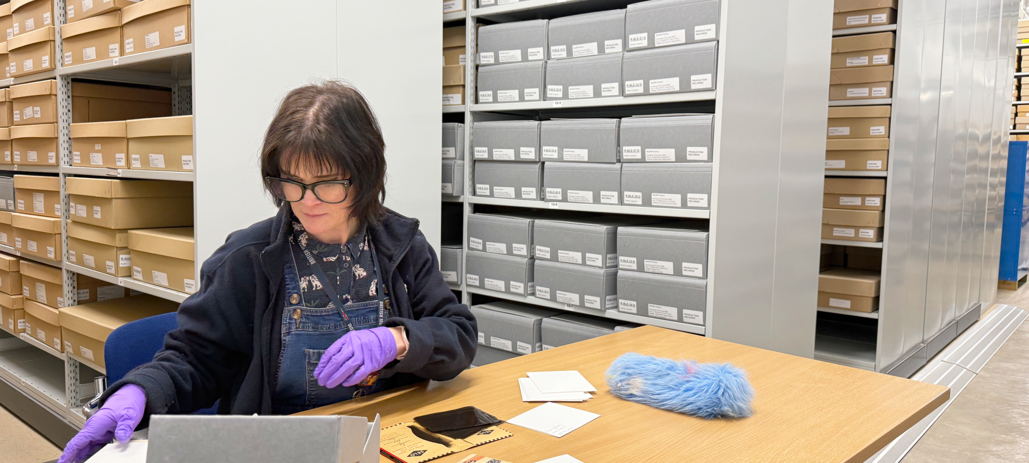 An Archive staff member sorting through photograph negatives inside the Archive, with lots of archive boxes on display in the background.